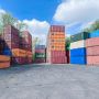 A storage area filled with stacked shipping containers of various colors under a partly cloudy sky.