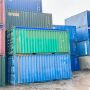 A stack of colorful shipping containers in a muddy environment. Various colors and labels are visible.